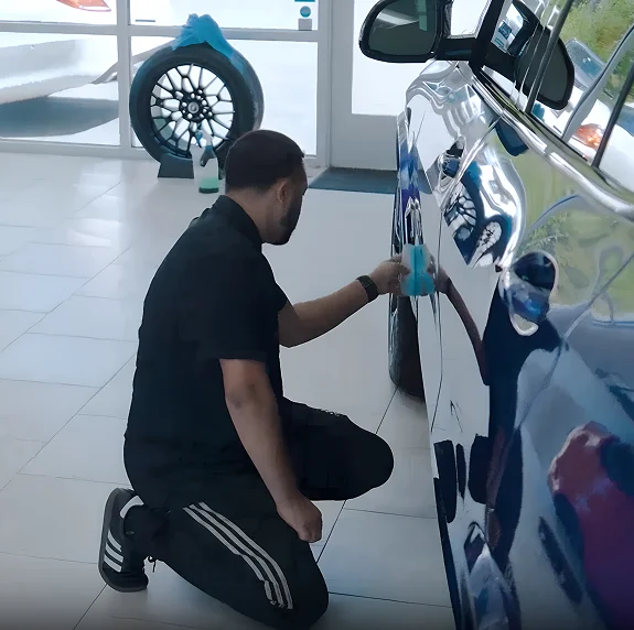 Technician applying ceramic coating to the side of a blue vehicle in a detailing bay