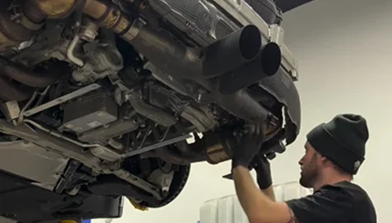 Technician installing a dual exhaust system underneath a raised vehicle