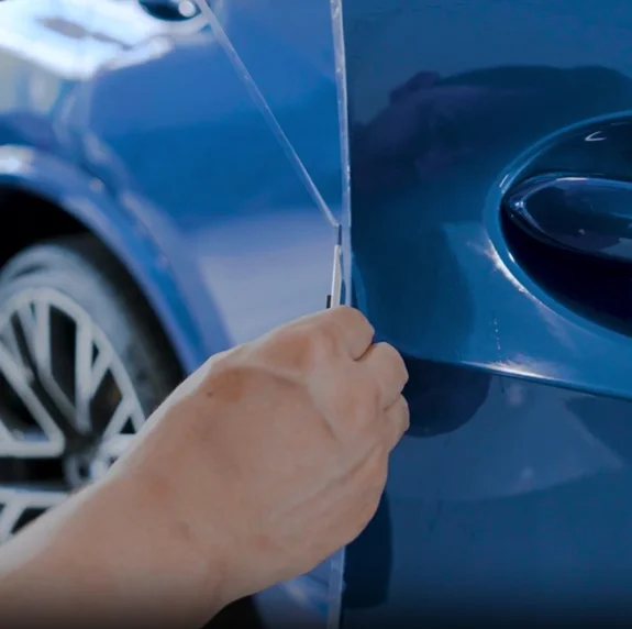 Installer applying clear paint protection film around the door handle of a blue vehicle