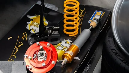 Yellow performance spring, shock, and suspension components installed beside a wheel